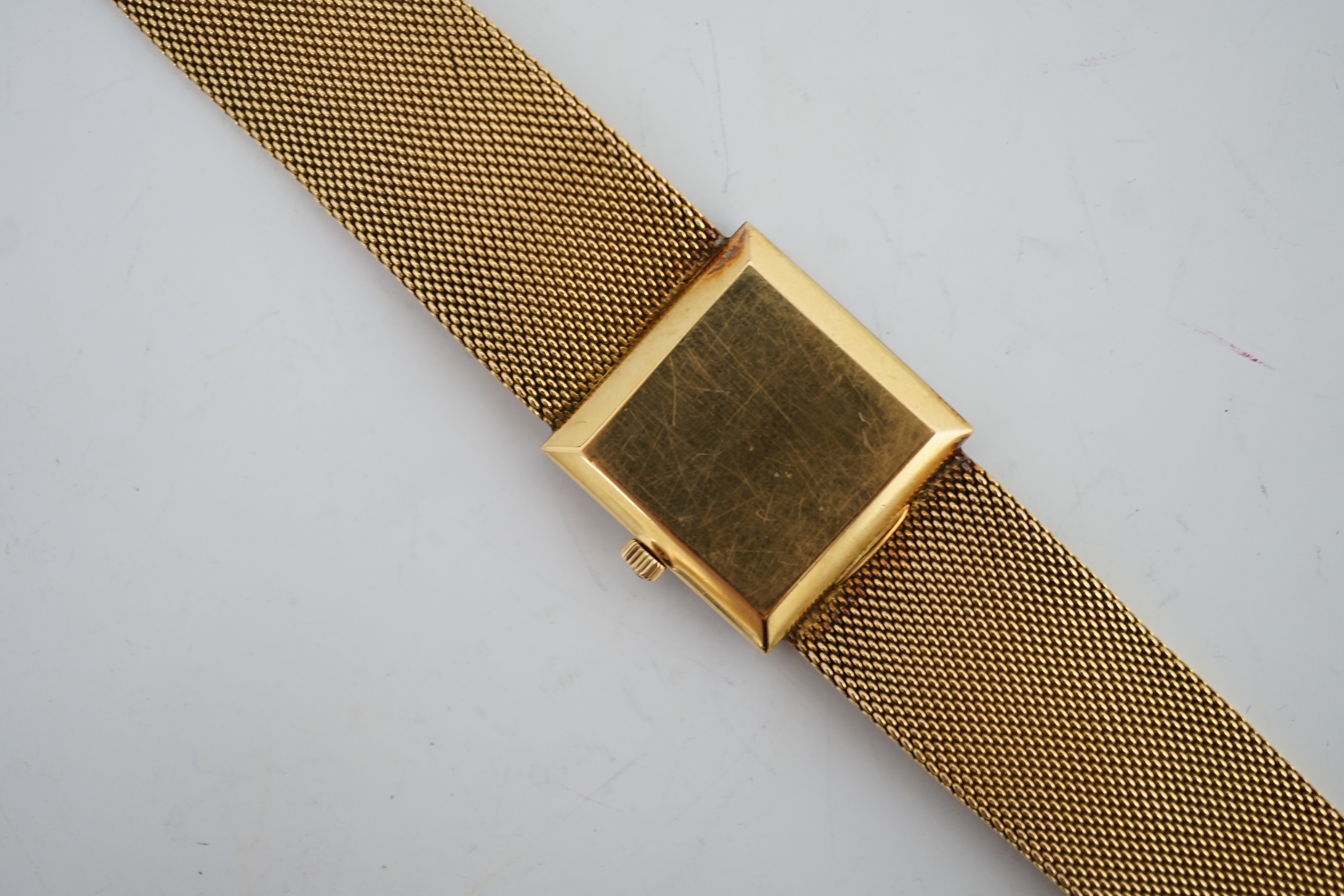 A gentleman's 18k gold Omega dress wrist watch, the square dial with baton markers, on integral textured close-link flexible Omega bracelet with clasp